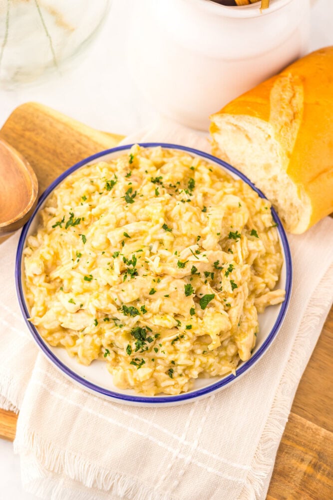 Slow cooker butter chicken and rice garnished with parsley, served in a blue-rimmed bowl with crusty bread