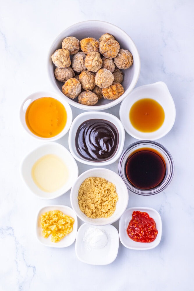 Slow cooker sticky sesame meatballs ingredients laid out including cooked meatballs, soy sauce, honey, sesame seeds, and other condiments