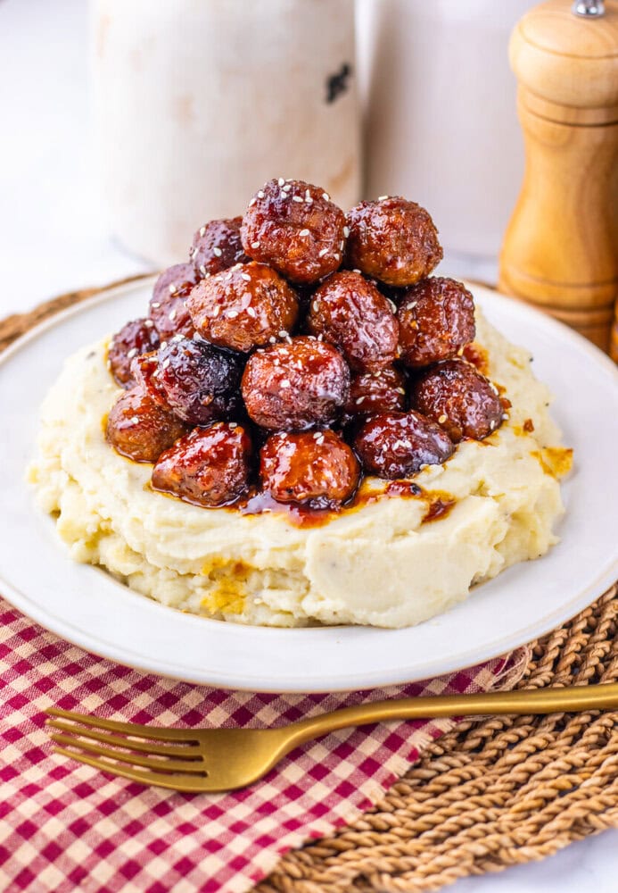 Slow cooker sticky sesame meatballs served over mashed potatoes with sesame seed garnish on a white plate