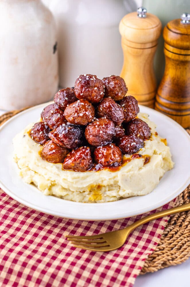 Slow cooker sticky sesame meatballs served over mashed potatoes on a white plate