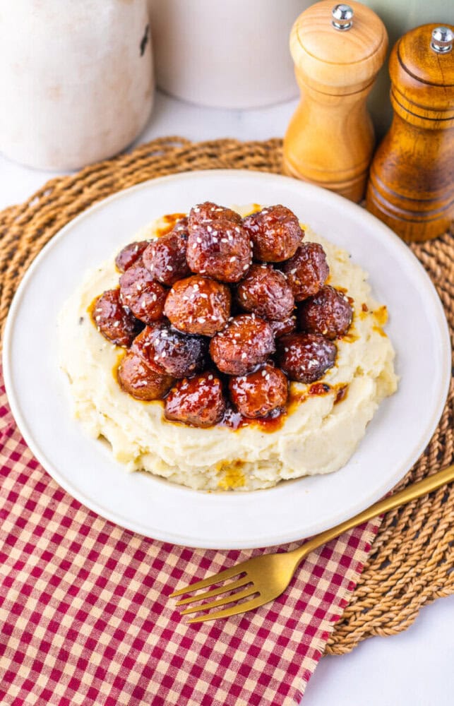 Slow cooker sticky sesame meatballs served over mashed potatoes on white plate with wooden salt and pepper shakers