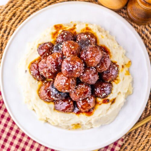 Slow cooker sticky sesame meatballs served over mashed potatoes on a white plate with wooden salt and pepper shakers