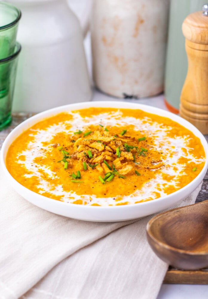 Creamy sweet potato soup in white bowl topped with roasted chickpeas, fresh green onions, and cream swirl