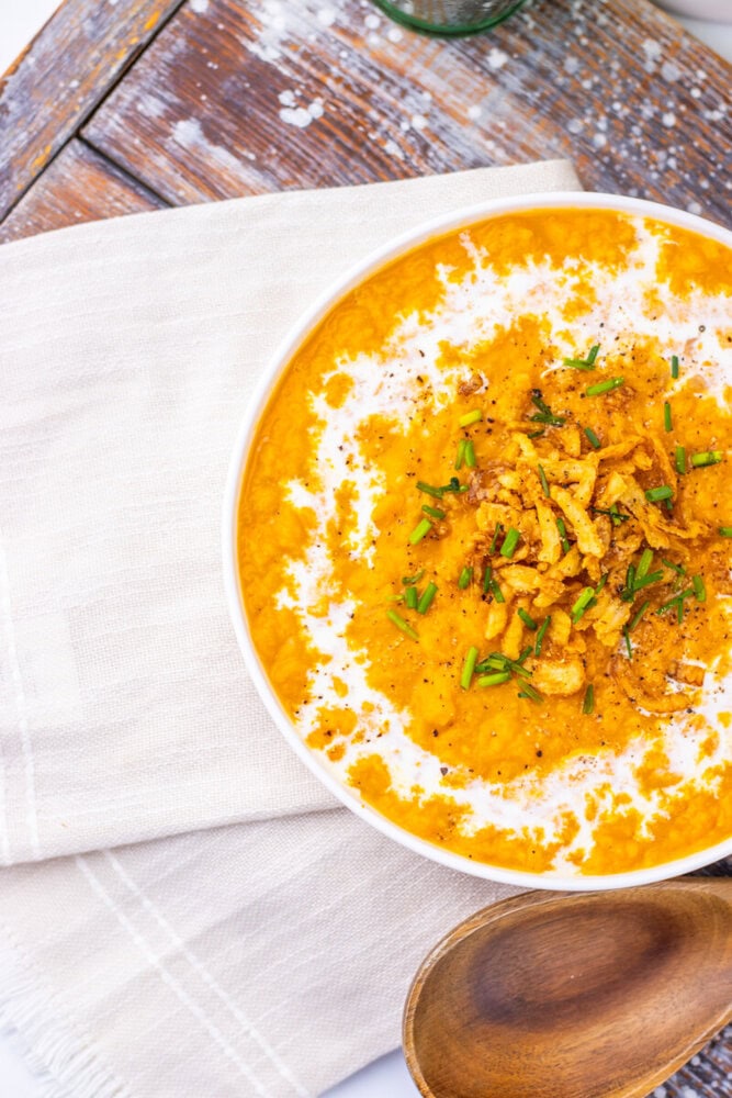 Creamy sweet potato soup with crispy onion garnish and chive in white bowl