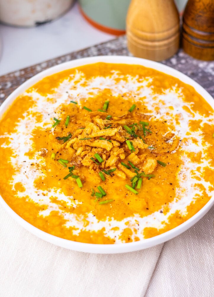 Creamy sweet potato soup with crispy chickpea garnish and green onion in white bowl