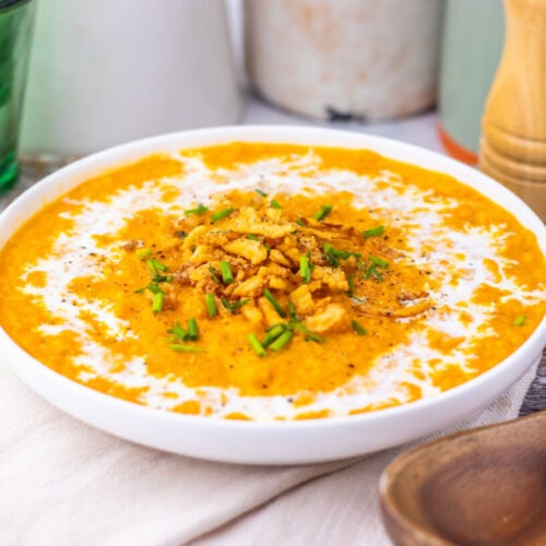 Creamy sweet potato soup in white bowl with crispy onion and green onion garnish