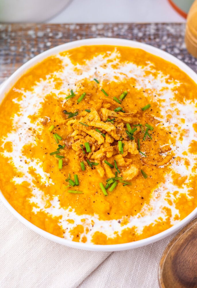 Creamy sweet potato soup in white bowl topped with fried onions, chives, and black pepper