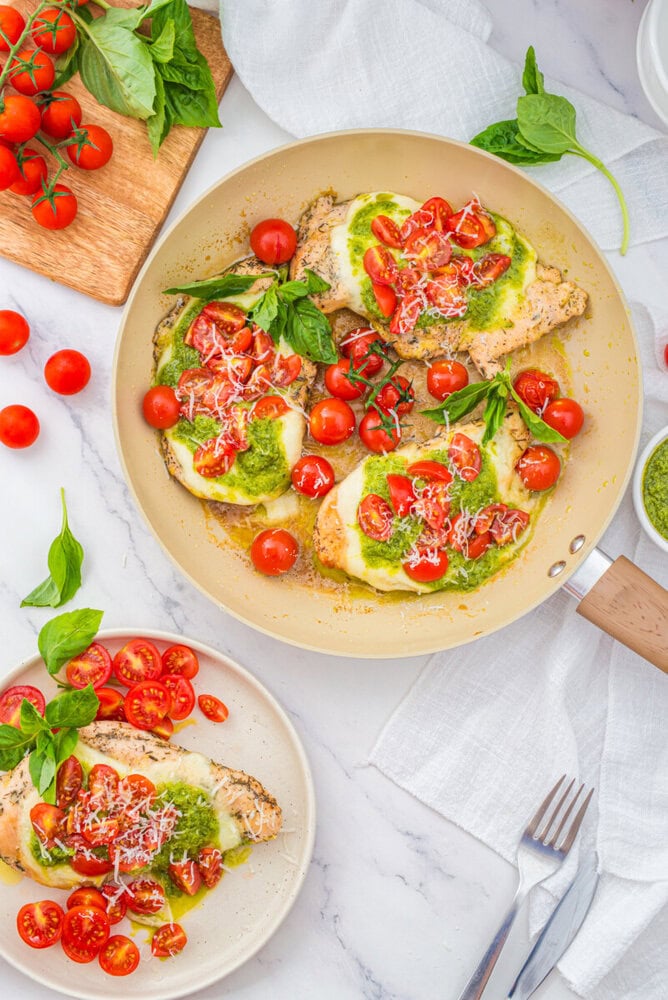 Chicken Margherita with fresh tomatoes, mozzarella, basil and pesto in a cream-colored pan, overhead flat lay view