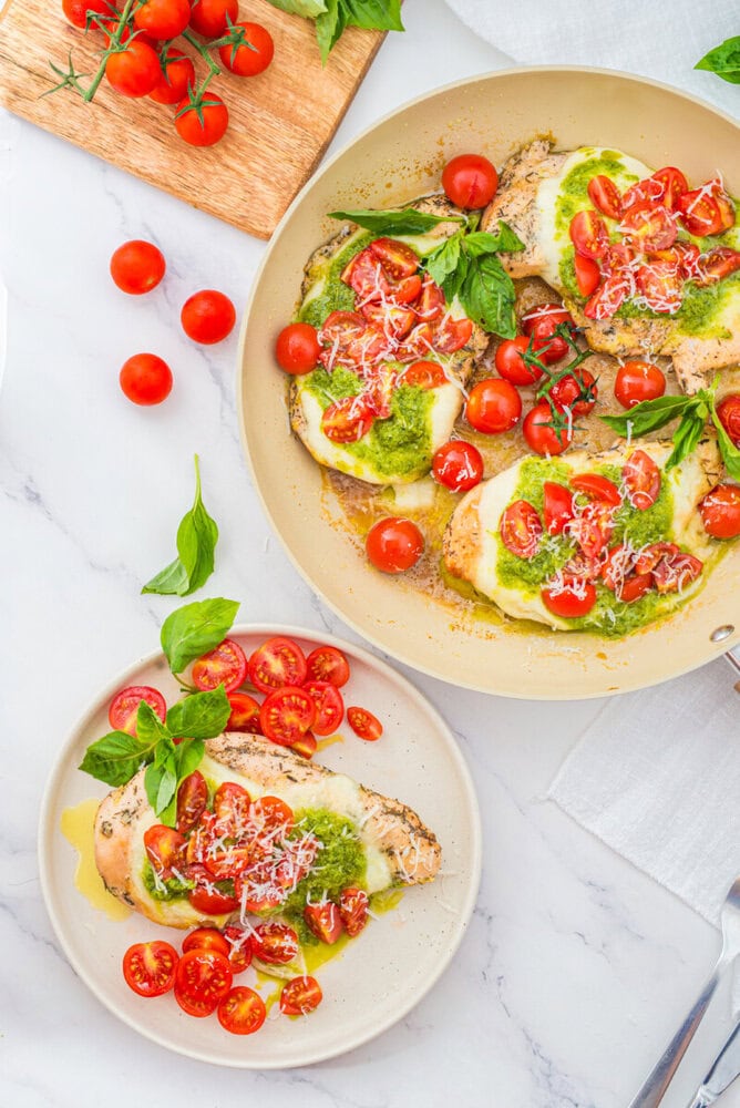 Chicken Margherita with fresh tomatoes, basil, mozzarella and pesto in skillet and plated, overhead shot