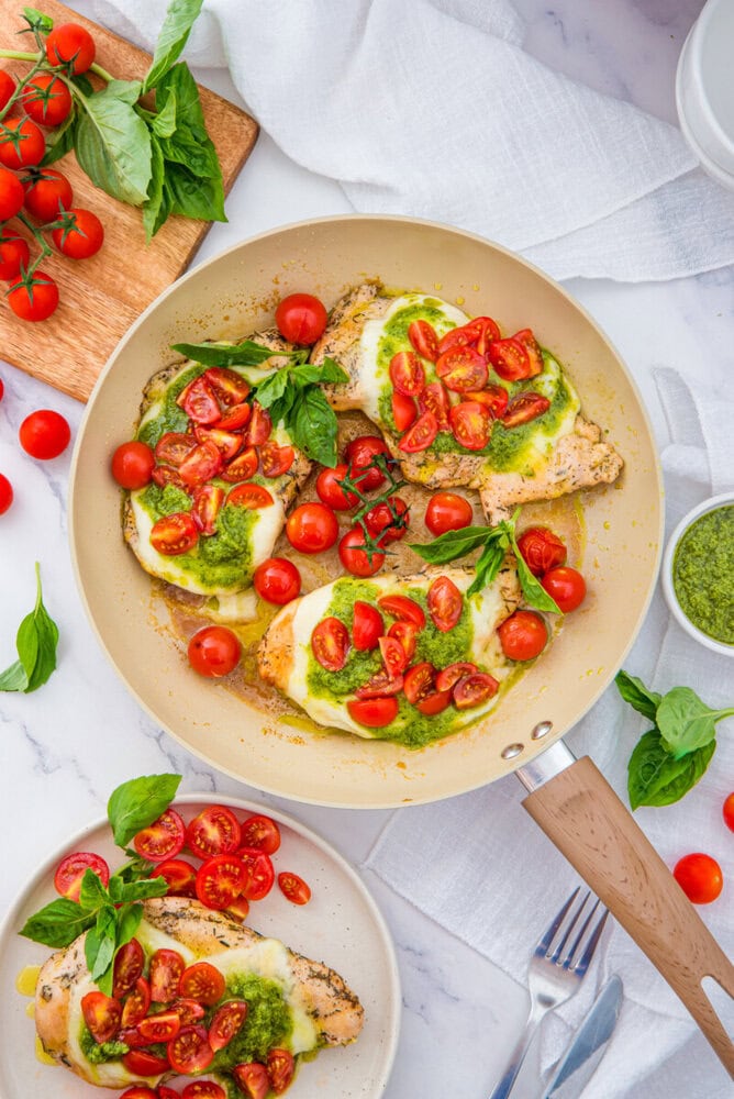Chicken Margherita with mozzarella, fresh tomatoes, basil and pesto in a cream pan, overhead flat-lay