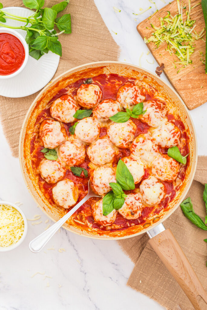 Chicken parmesan meatballs in tomato sauce with melted cheese and fresh basil in a round baking pan