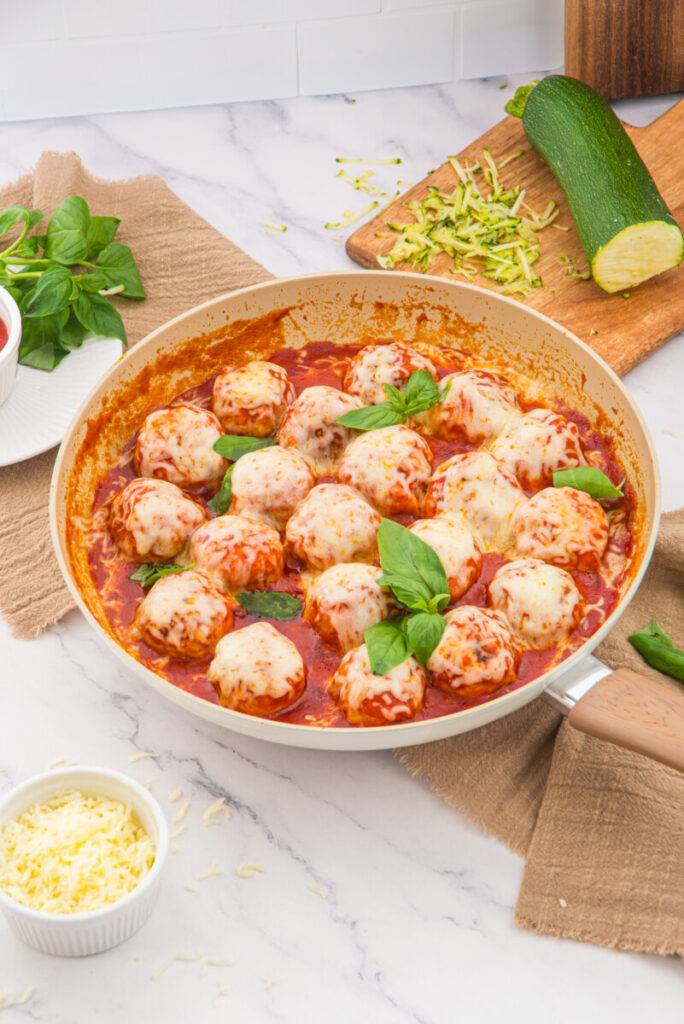 Chicken parmesan meatballs in tomato sauce with fresh basil garnish in white skillet