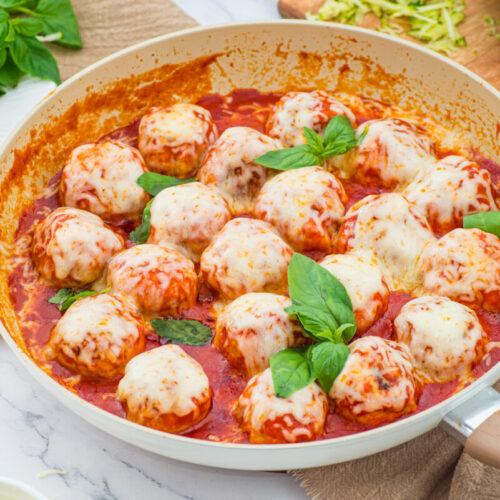 Chicken parmesan meatballs in tomato sauce with fresh basil in a white skillet
