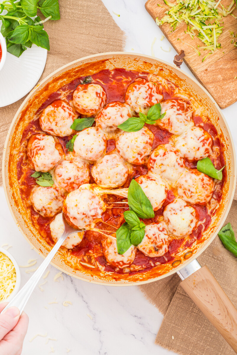 Chicken parmesan meatballs in tomato sauce with melted cheese and basil in a skillet, overhead view