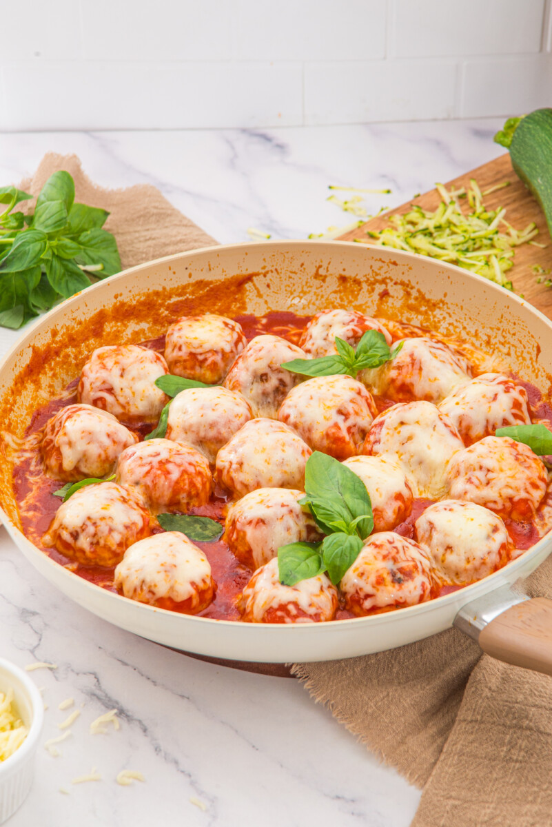 Chicken parmesan meatballs in red tomato sauce with melted cheese and fresh basil garnish in a white skillet