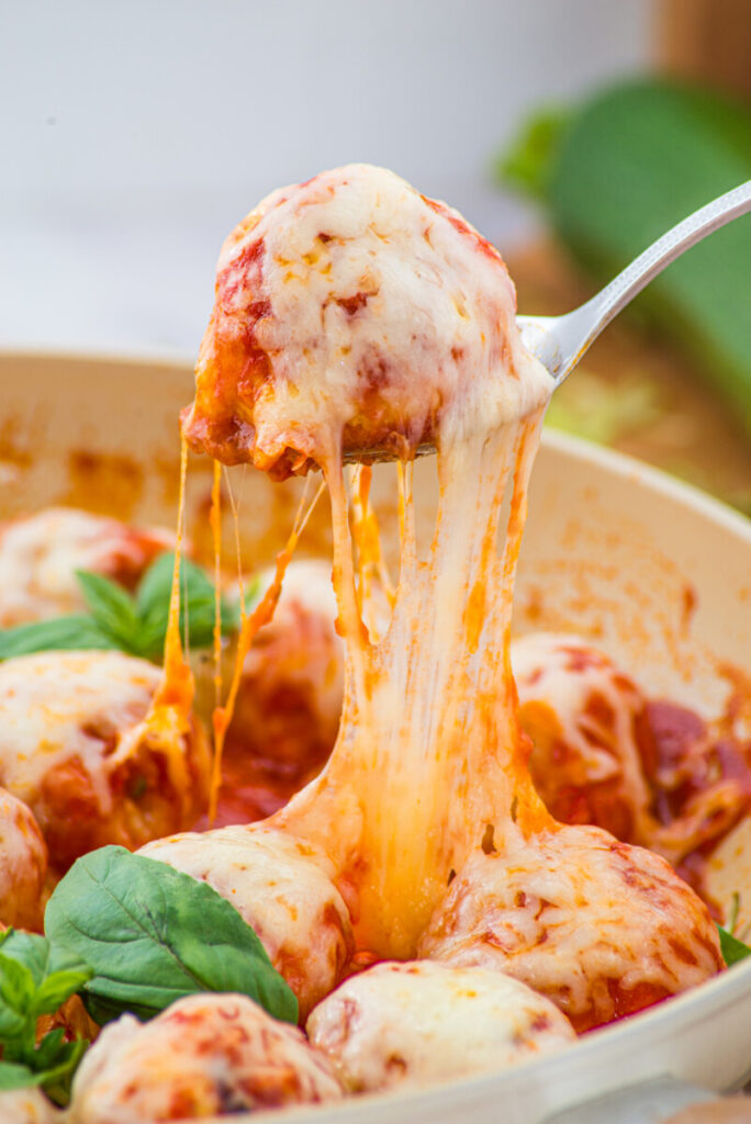 Chicken Parmesan Meatball with melted cheese being lifted on a spoon, demonstrating the stretchy cheese pull and golden coating
