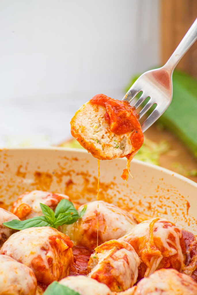 Chicken Parmesan Meatballs with melted cheese on fork, baked in tomato sauce