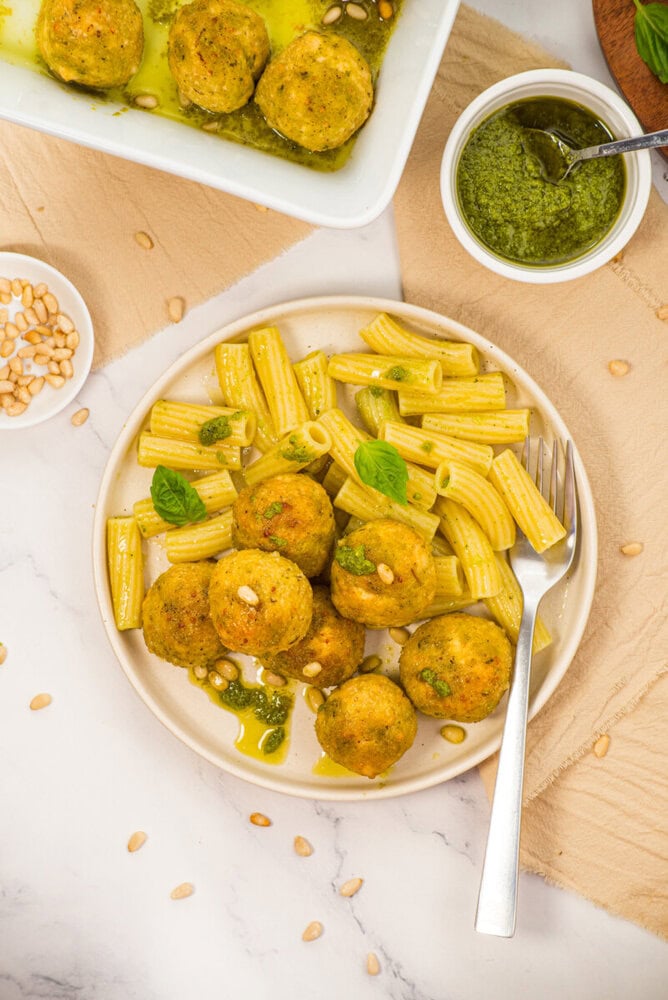 Chicken pesto meatballs with penne pasta garnished with basil and pine nuts, served with homemade pesto sauce