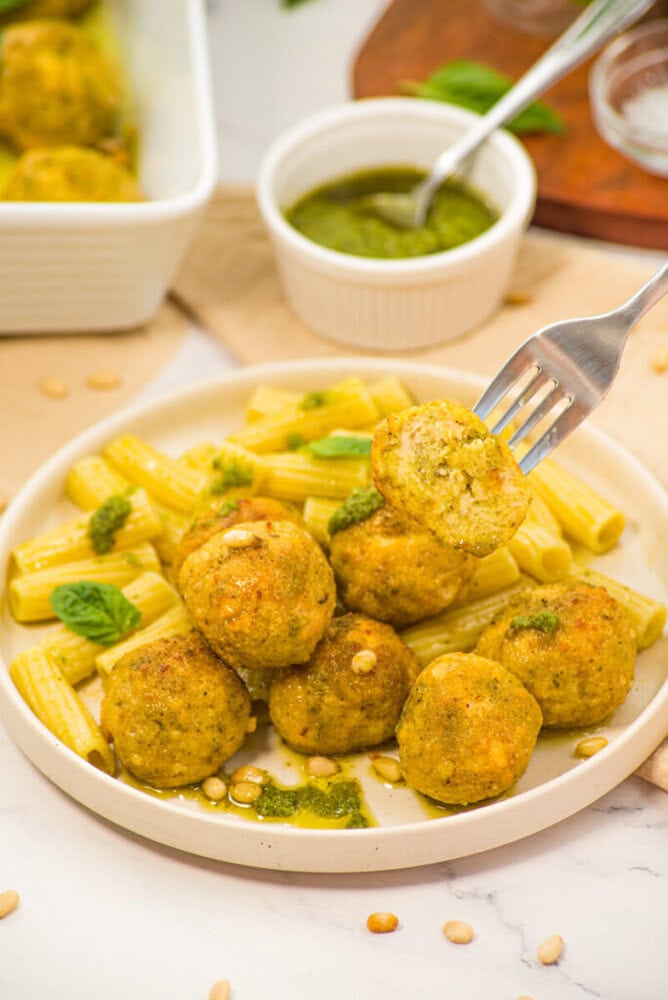 Chicken pesto meatballs with penne pasta and fresh basil garnish on white plate