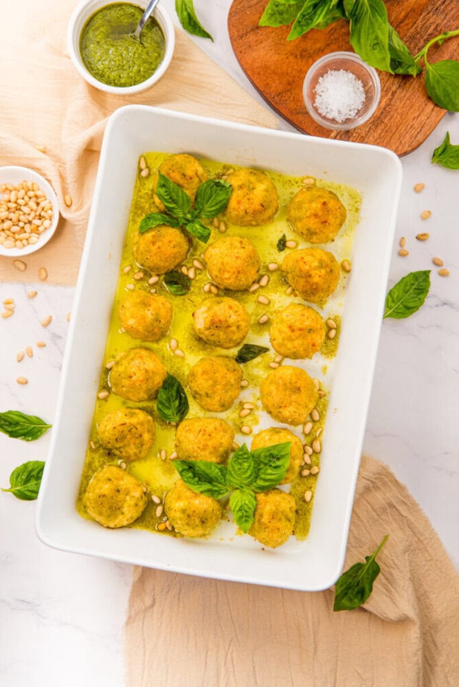 Chicken pesto meatballs in pesto sauce with pine nuts and basil garnish, ready to serve