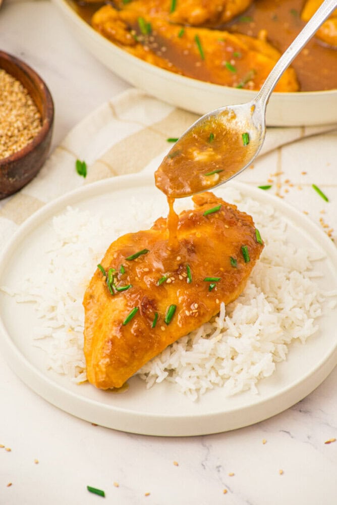 Honey butter chicken served over white rice with sesame seeds and green onions, sauce being drizzled on top
