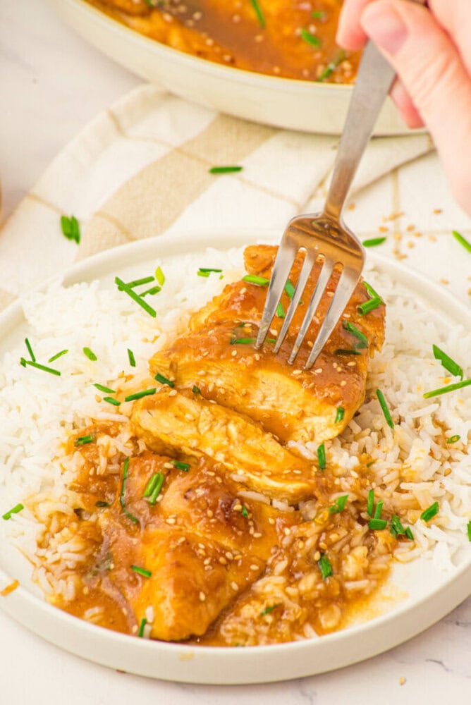 Honey butter chicken served over white rice with green chives garnish on white plate
