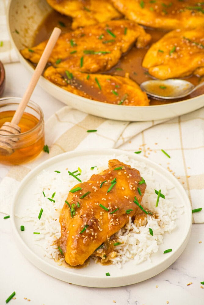 Honey butter chicken breast with sesame seeds served over rice on a white plate