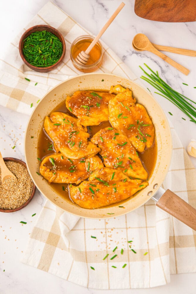 Honey butter chicken with chives in a pan, overhead view with honey, green onions, and sesame seeds