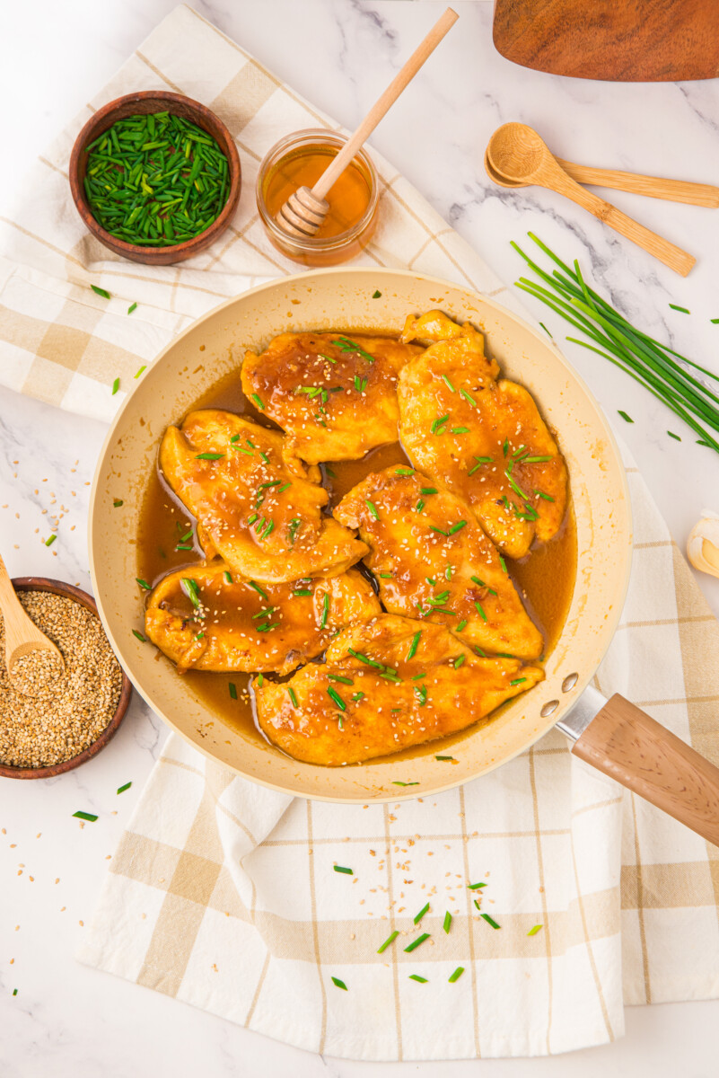 Honey butter chicken with chives in a pan, overhead view with honey, green onions, and sesame seeds