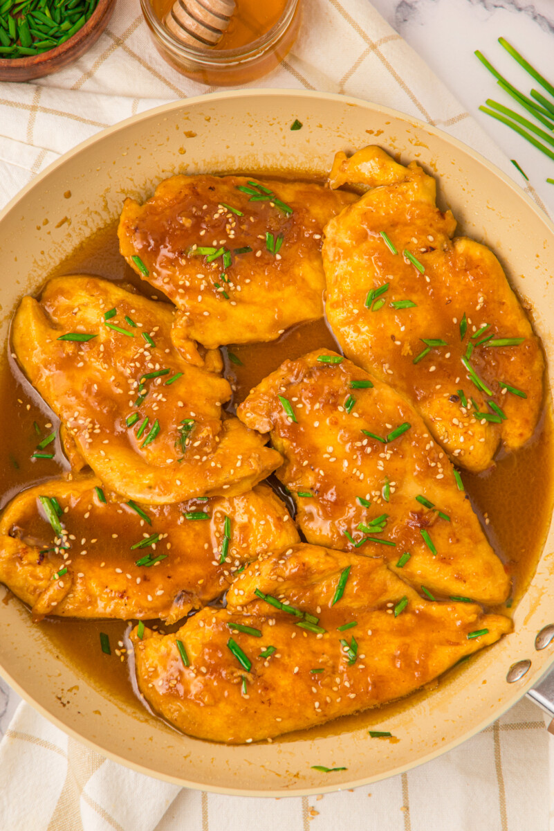 Honey butter chicken breasts with golden glaze and chives in a skillet