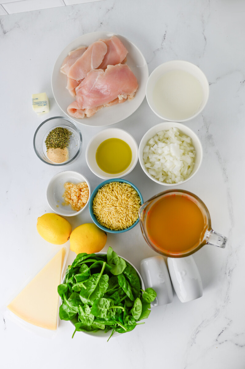 Ingredients for Creamy Lemon Parmesan Chicken Orzo arranged overhead on marble, including raw chicken, orzo pasta, fresh spinach, lemon, and seasonings