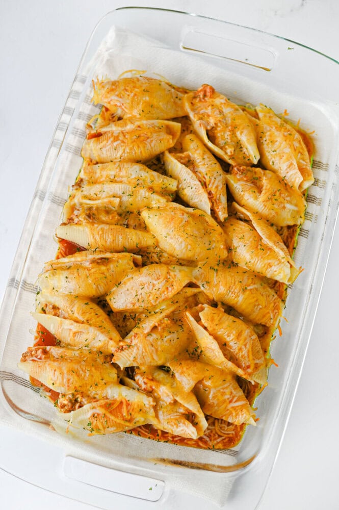 Cheesy taco stuffed shells baked in glass dish with golden brown tops and herb garnish
