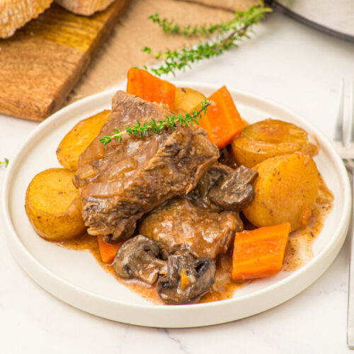 Slow cooker beef pot roast with roasted potatoes and carrots garnished with thyme on a white plate