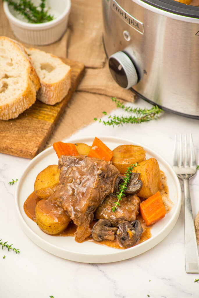 Slow cooker beef pot roast with roasted vegetables and fresh thyme garnish on white plate