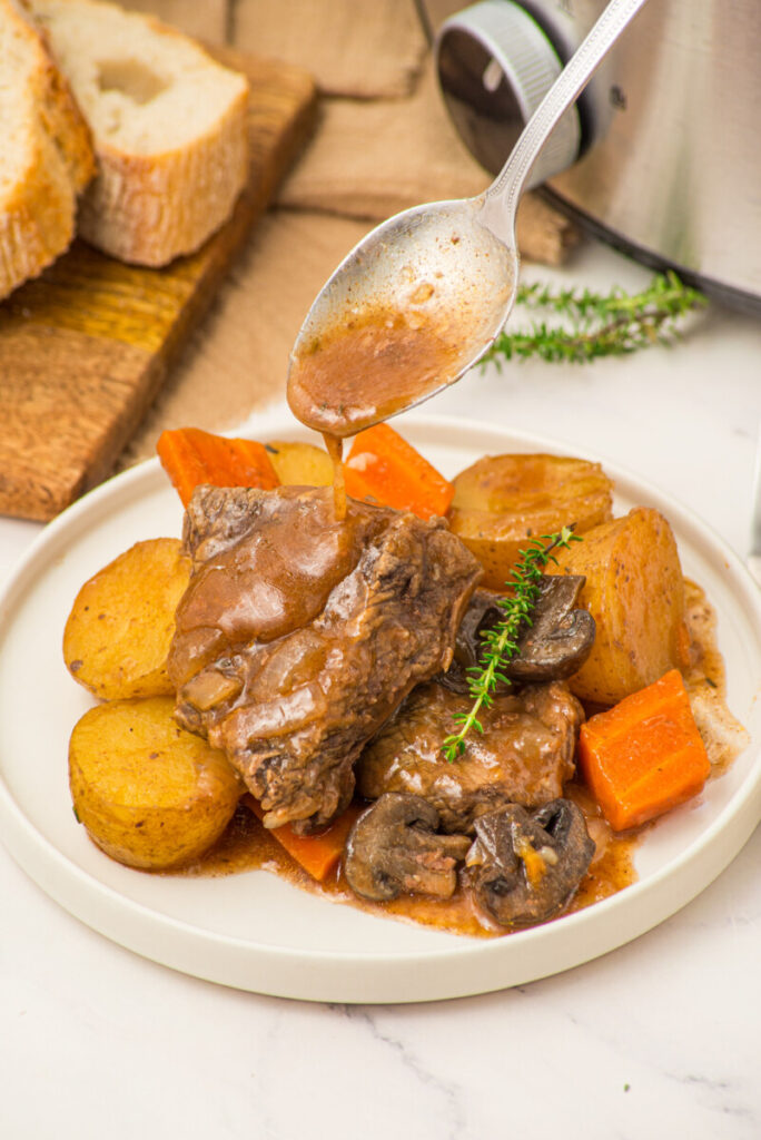 Slow cooker beef pot roast with potatoes, carrots, and gravy drizzle on white plate