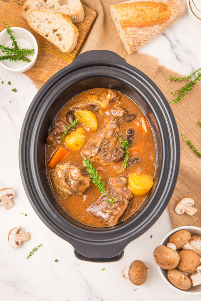 Slow cooker beef pot roast with potatoes, carrots and herbs in black oval cooker