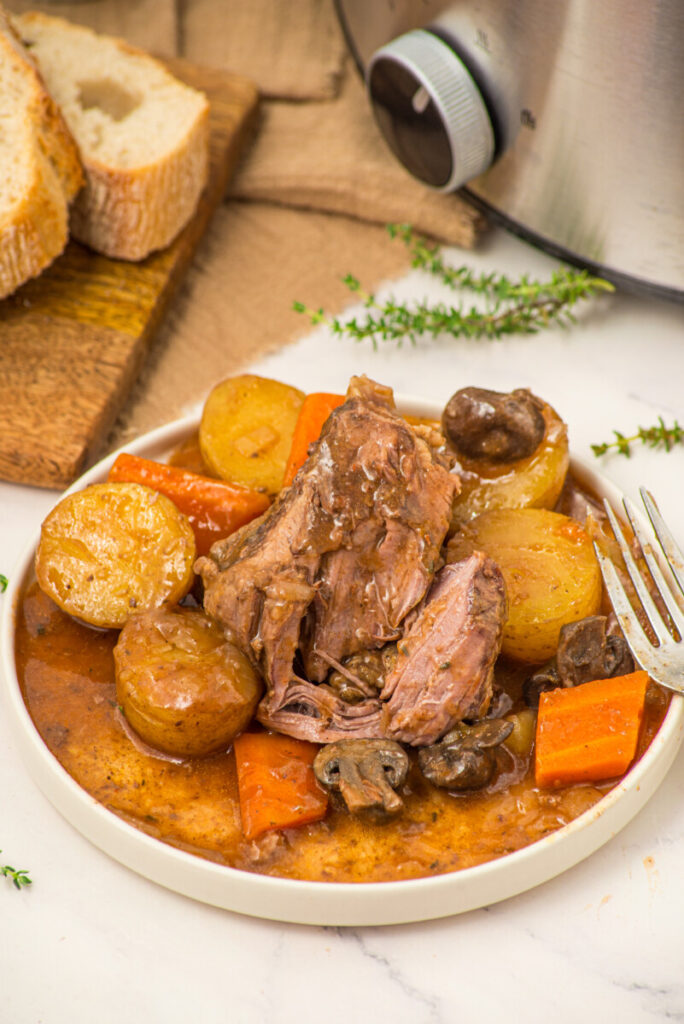 Slow cooker beef pot roast with potatoes, carrots and mushrooms in gravy on white plate