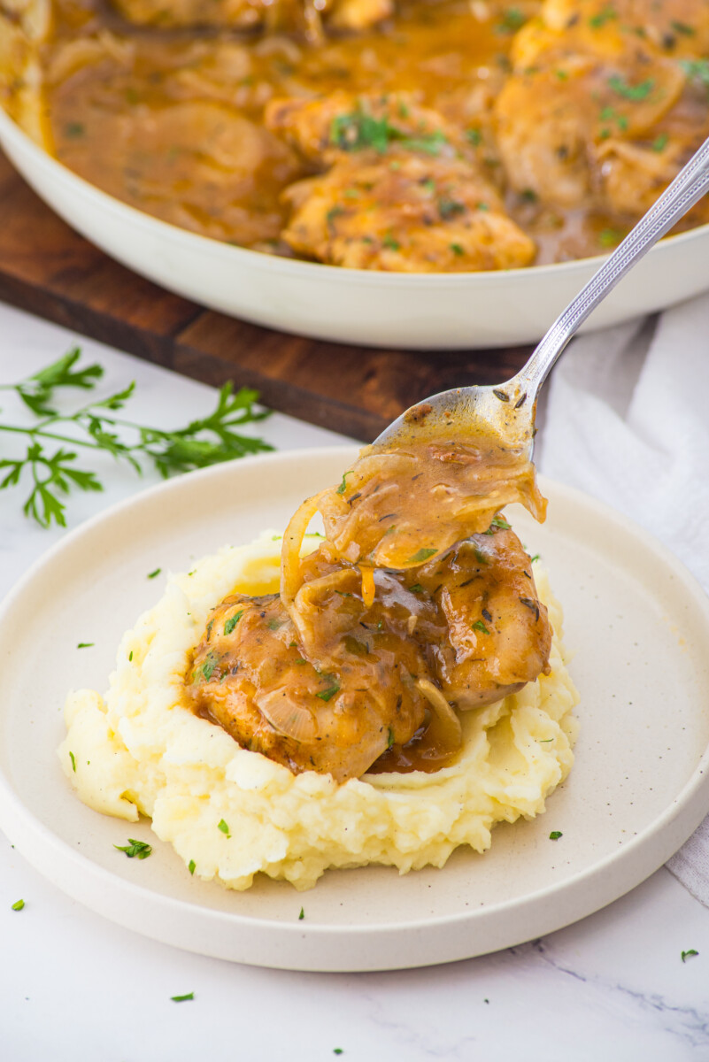 Smothered chicken with caramelized onions served over mashed potatoes with fresh parsley garnish