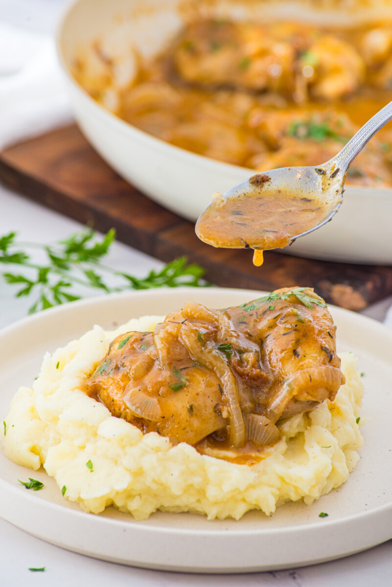 Smothered chicken with caramelized onions and gravy served over mashed potatoes on a white plate