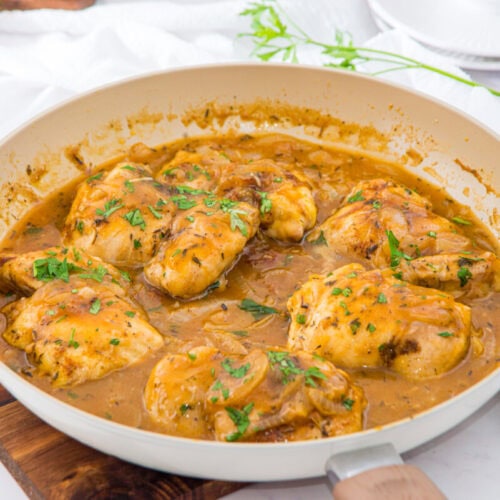 Smothered chicken thighs in creamy brown sauce with parsley garnish in white ceramic pan