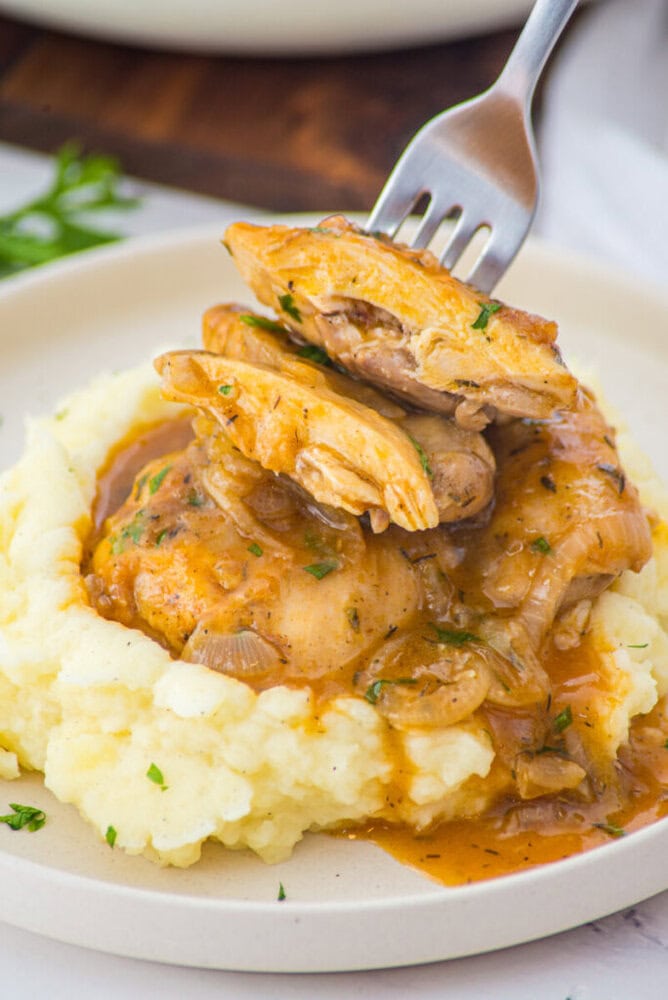 Smothered chicken with caramelized onions and mashed potatoes plated on white dish with fork