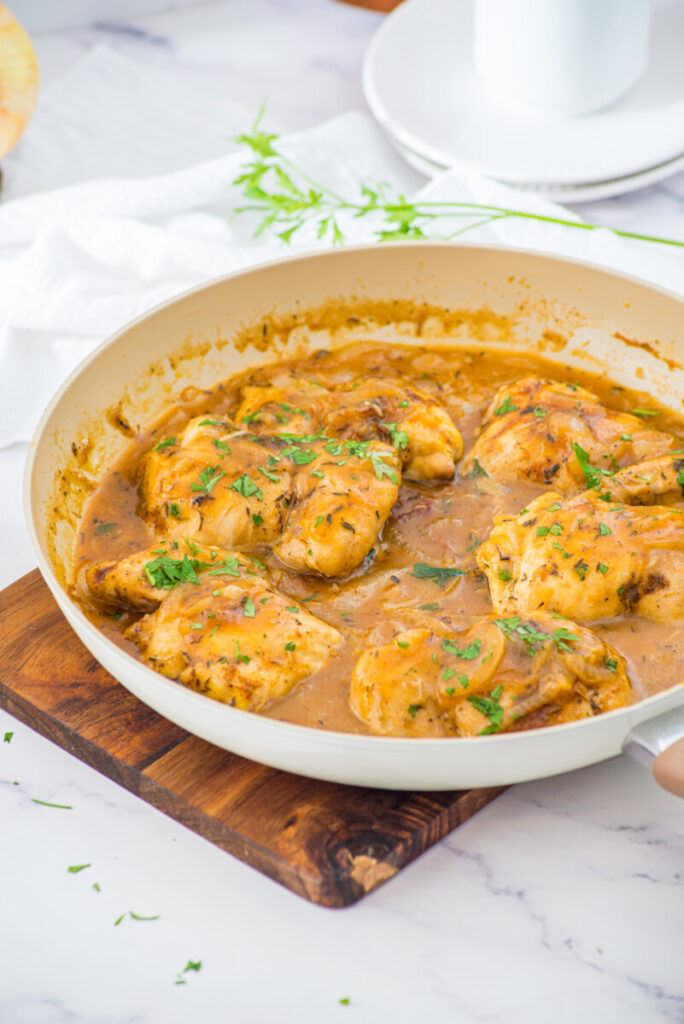 Smothered chicken with creamy gravy sauce in white pan garnished with fresh chives