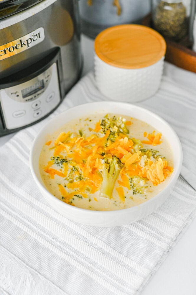 Crock Pot broccoli cheddar soup in white bowl with cheese and broccoli garnish