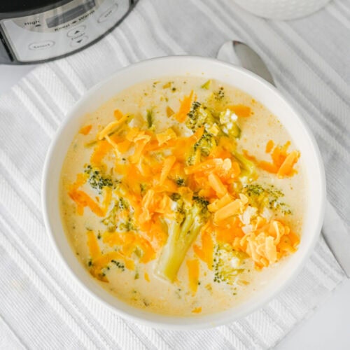 Creamy crock pot broccoli cheddar soup garnished with melted cheese and parsley in a white bowl