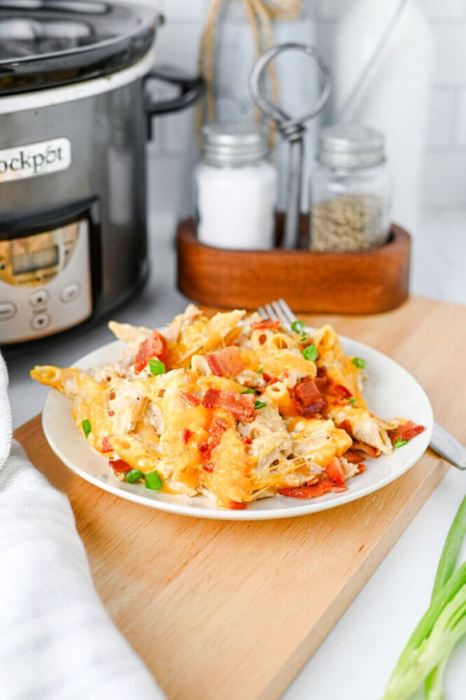 Crockpot crack chicken pasta with bacon and green onions on white plate with slow cooker in background