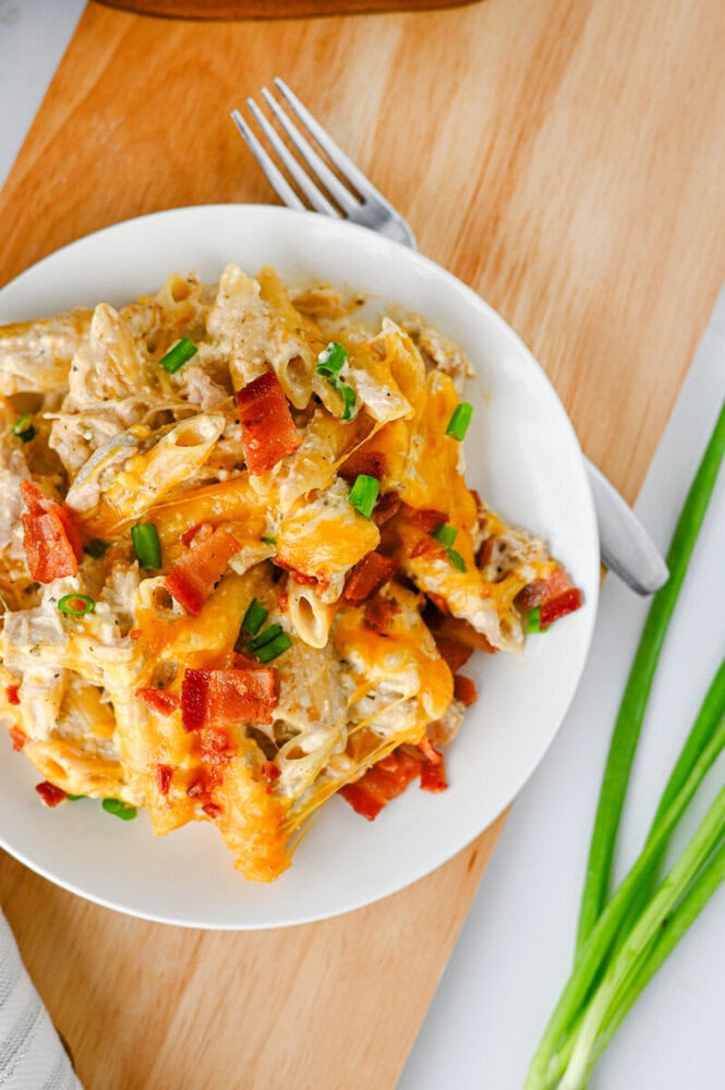 Crockpot crack chicken pasta with cheddar cheese, bacon bits, and green onions on a white plate