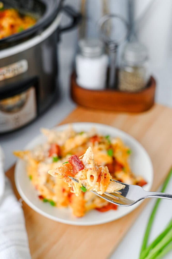 Crockpot crack chicken pasta with bacon and cheese on white plate with fork, slow cooker in background
