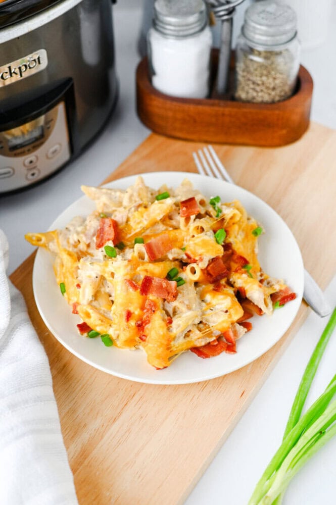 Crockpot crack chicken pasta with bacon and cheese garnished with red peppers and green onions on white plate