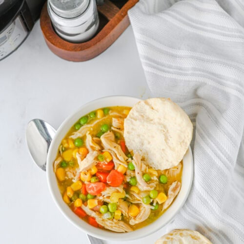 Crock pot chicken and biscuits stew with corn, peas, carrots and shredded chicken in creamy broth served with fluffy biscuits