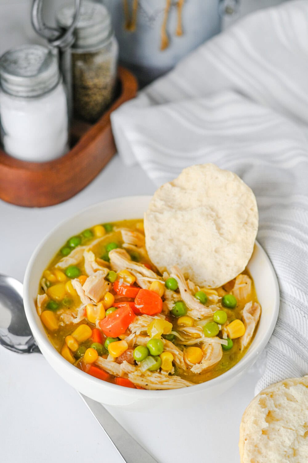 Crock Pot chicken and biscuits with mixed vegetables and golden broth in white bowl with buttermilk biscuit